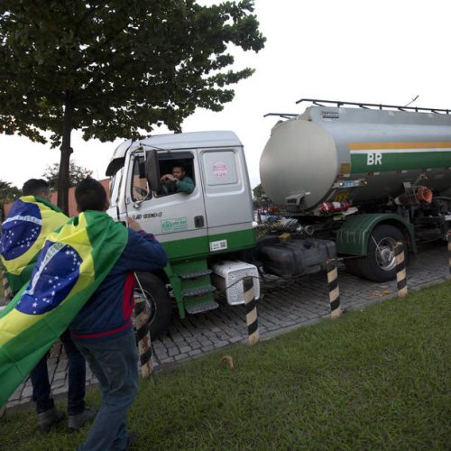 Demonstrators with Brazil's national flag on their shoulders stand near a truck loaded with fuel as it leaves the Petrobras refinery in Duque de Caxias, Brazil, Friday, May 25, 2018. A nationwide strike by thousands of truckers brought much of Latin America's largest nation to a halt on Friday, prompting Brazilian President Michel Temer to authorize the military to use force in removing drivers and their parked vehicles from highways and other roads. (AP Photo/Silvia Izquierdo)